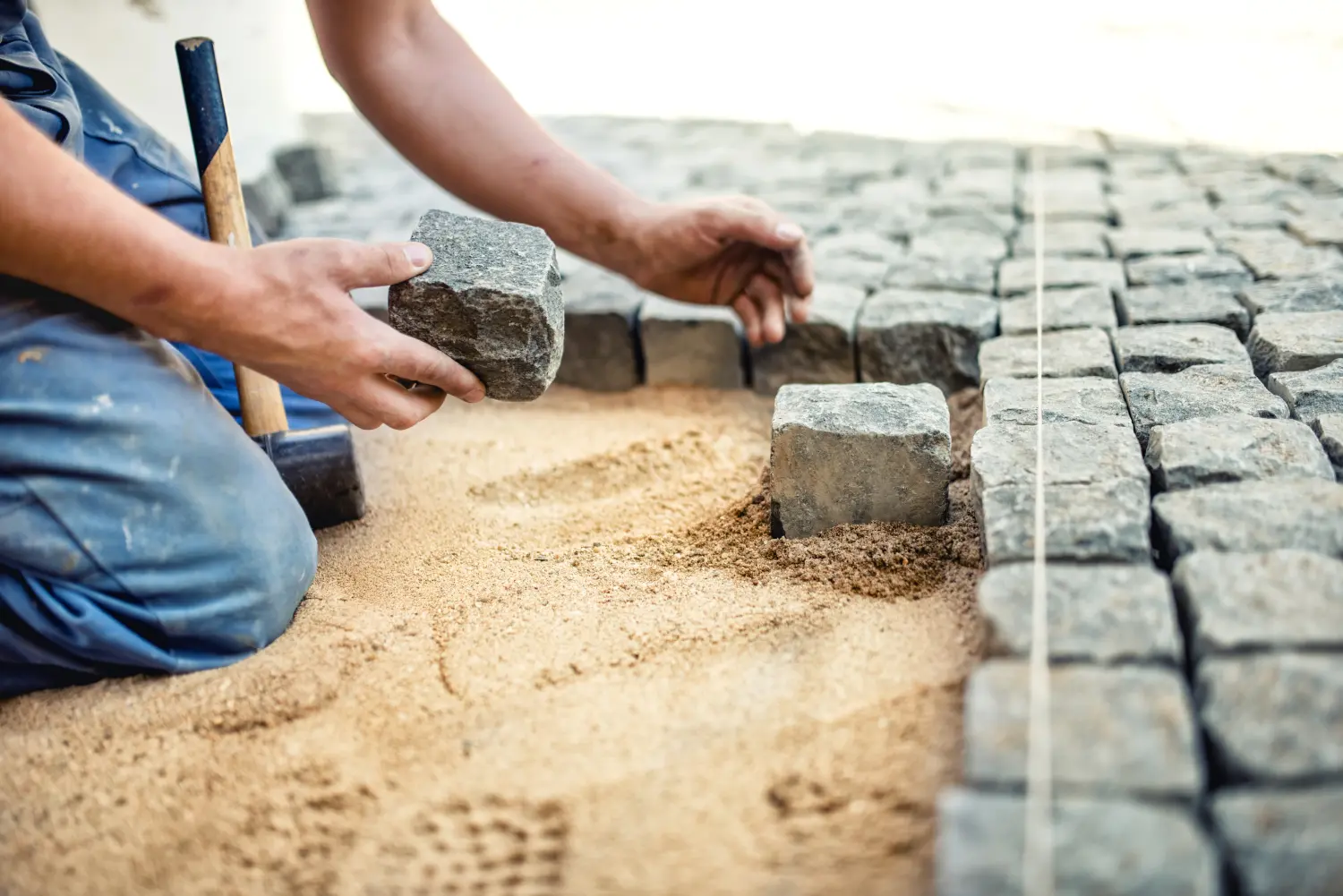 Bauarbeiter beim Verlegen von Steinplatten in Sand für Pflaster, Terrasse. Arbeiter beim Verlegen von Granit-Pflastersteinen auf einer Terrasse